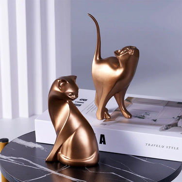 Two Golden Couples Cat Figurines by KittyNook Cat Co. on a black table with books, in a chic modern white setting.