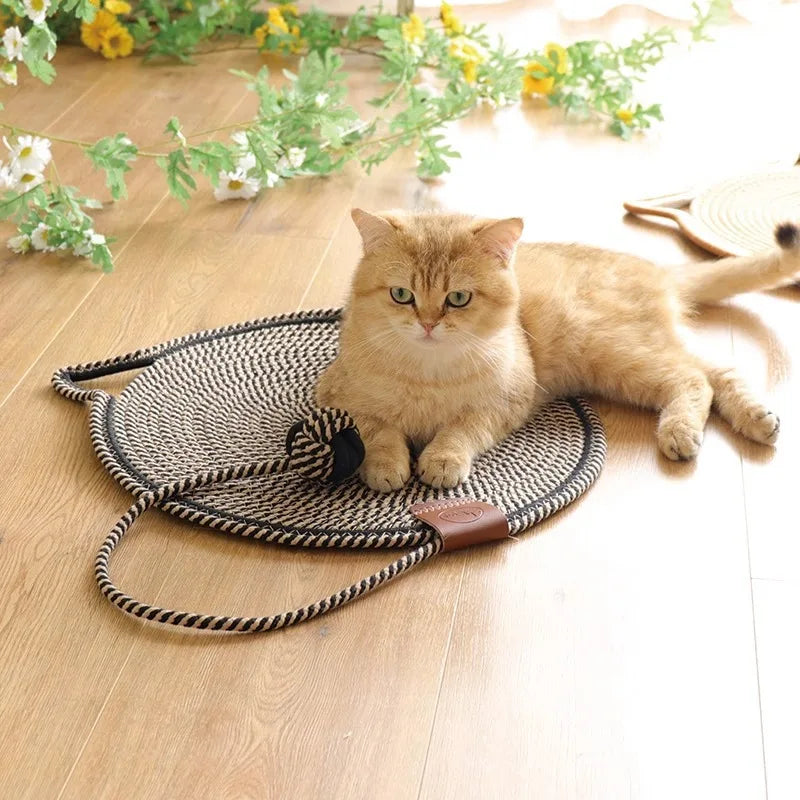 A fluffy orange cat relaxes on the Tails Cat Scratching Mat by KittyNook, surrounded by green leaves and yellow flowers.