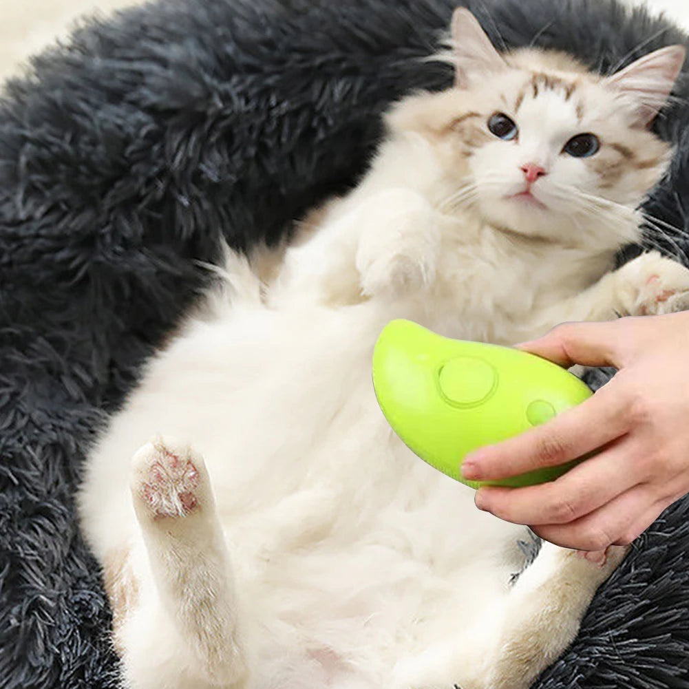 Someone uses the KittyNook Cat Co. Electric Cat Grooming Brush on a fluffy white cat lying on a dark furry bed.