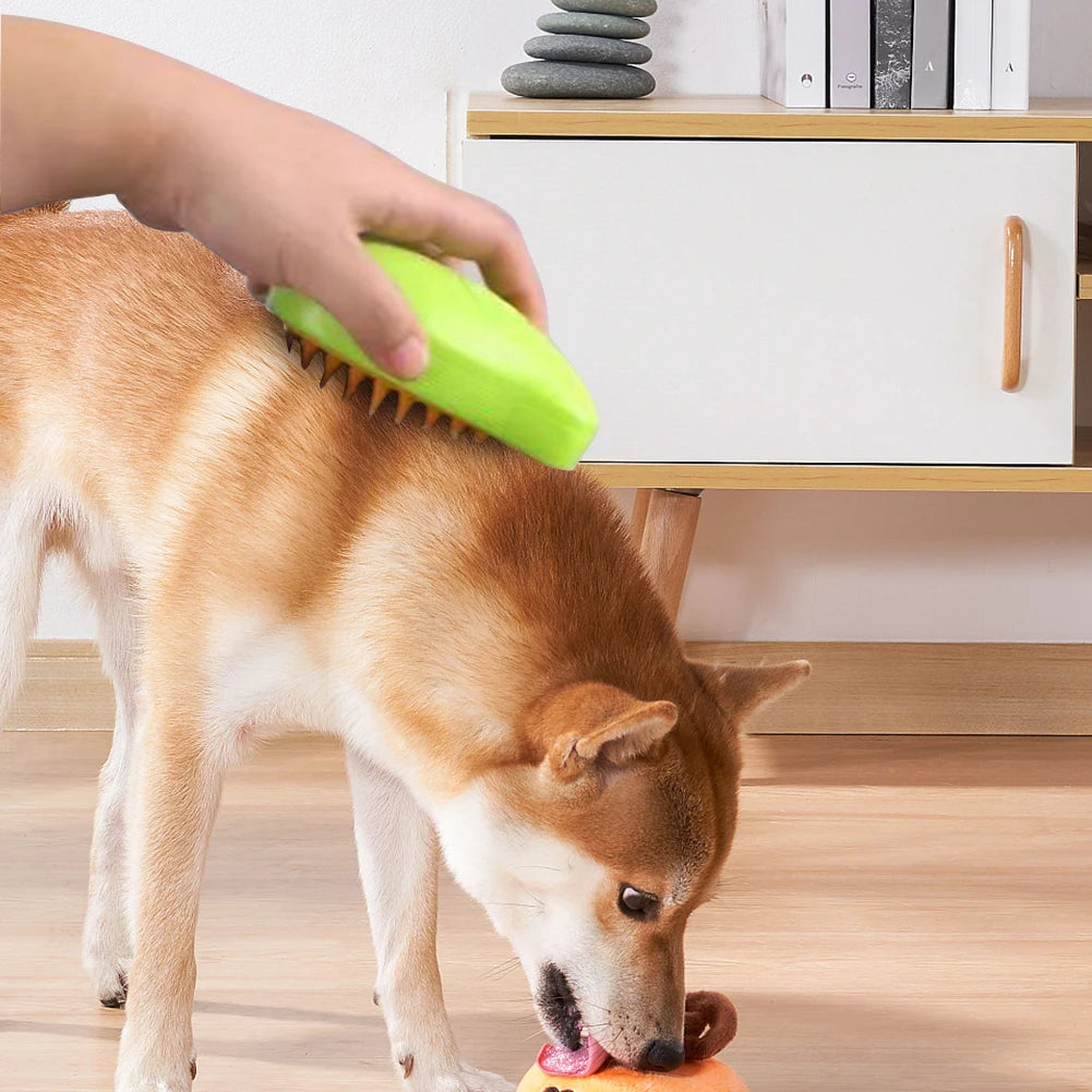 A hand uses the KittyNook Cat Co. Electric Cat Grooming Brush on a Shiba Inu chewing a toy indoors.