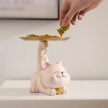 A hand places candy on the Chic Cat Metal Key Tray by KittyNook Cat Co., shaped like a smiling cat, on a white surface.