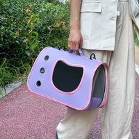 Thumbnail for Person holding a KittyNook Cat Co. Portable Pet Carrier Bag with mesh window, standing on a red path near greenery.