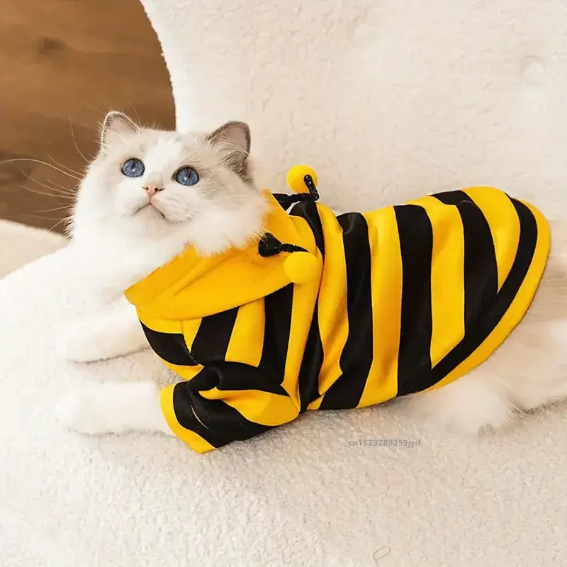 A cat in the KittyNook Cat Co. Cute Bee Costume lies on a white fuzzy surface.