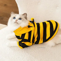 Thumbnail for A cat in the KittyNook Cat Co. Cute Bee Costume lies on a white fuzzy surface.