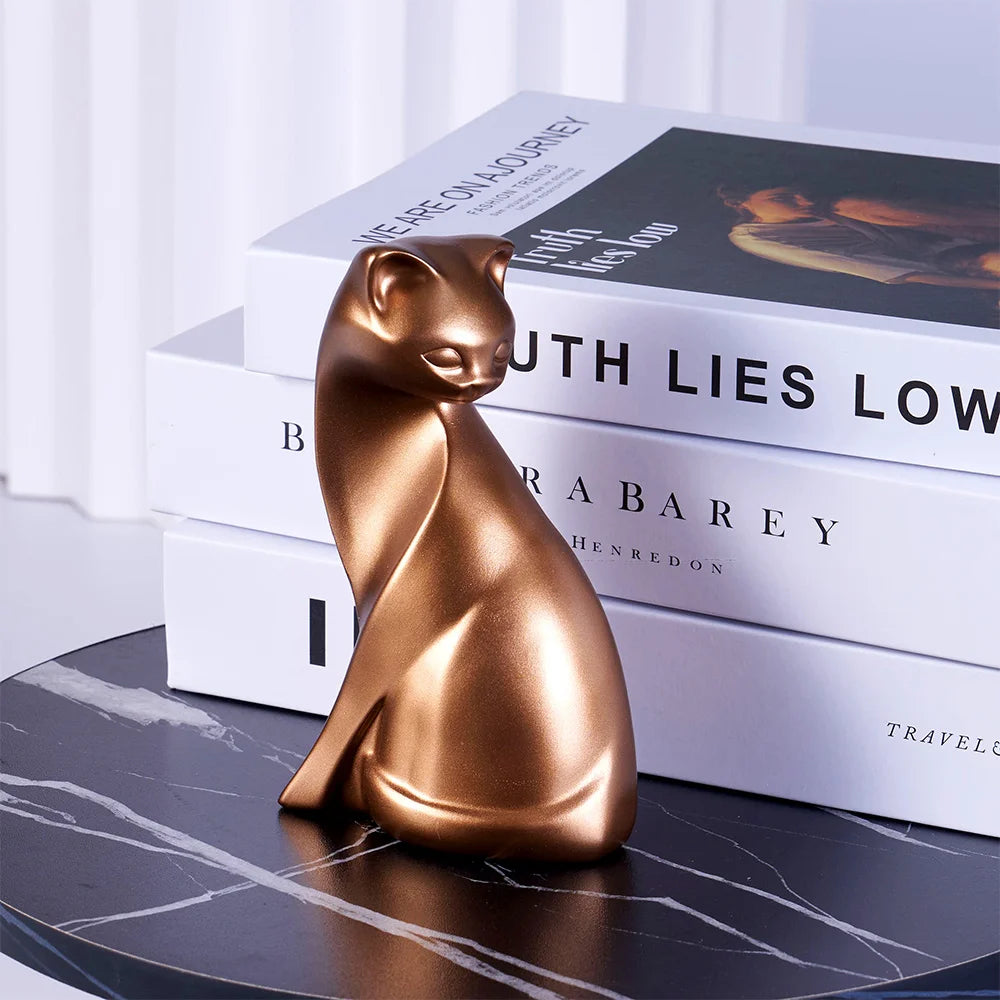 The Golden Couples Cat Figurine by KittyNook Cat Co. sits on a round black table before stacked hardcover books.