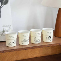 Thumbnail for Four KittyNook Cat Co. Cute Illustrated Ceramic Cat Mugs are lined up on a shelf next to a lamp and book.