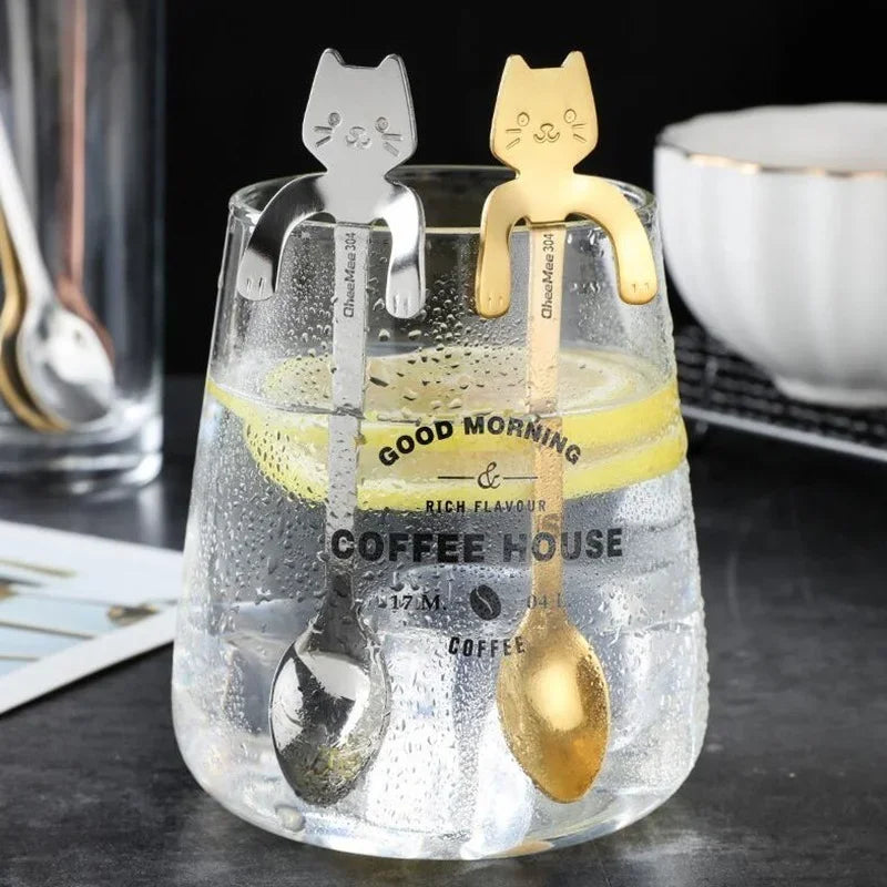 Two Cat Cling Stainless Steel Mug Spoons from KittyNook Cat Co. hang like cats on a glass with lemon slices.
