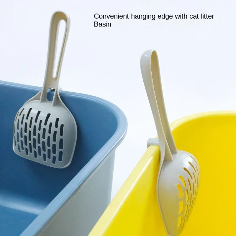 Two KittyNook Cat Co. Curved Cat Litter Shovels hang on blue and yellow boxes for easy, odor-free litter cleaning.