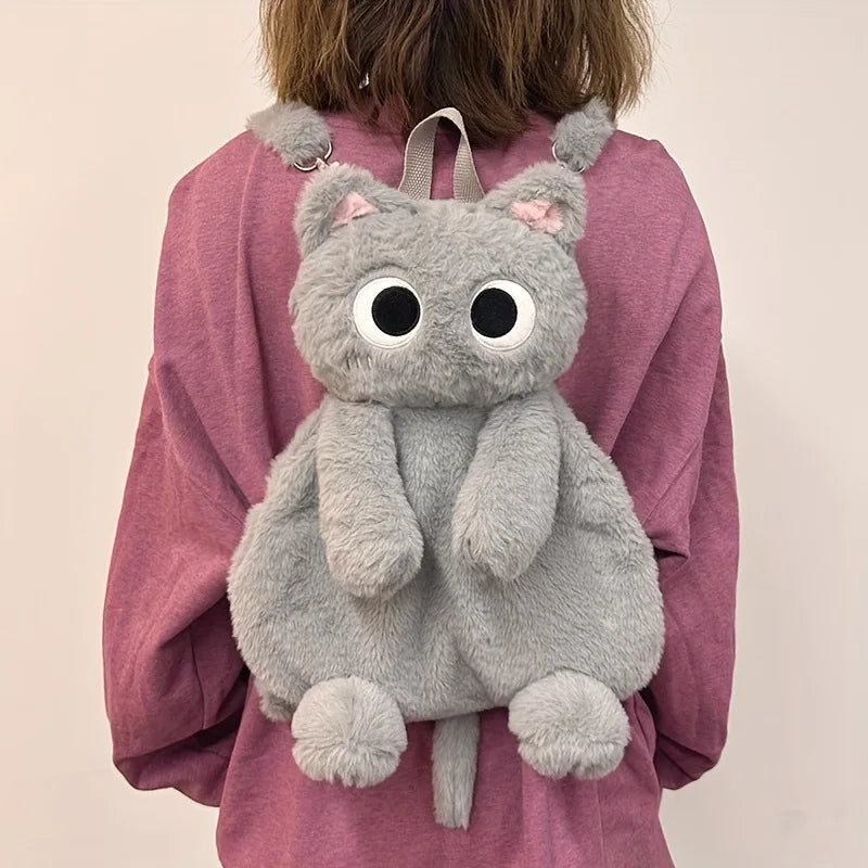 Person wearing The Cute Big Eyes Plush Backpack by KittyNook Cat Co. over a pink sweater.