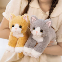 Thumbnail for A person hugs two Snuggle Soft Cat Plush Dolls by KittyNook Cat Co.—one orange & white, the other gray & white.