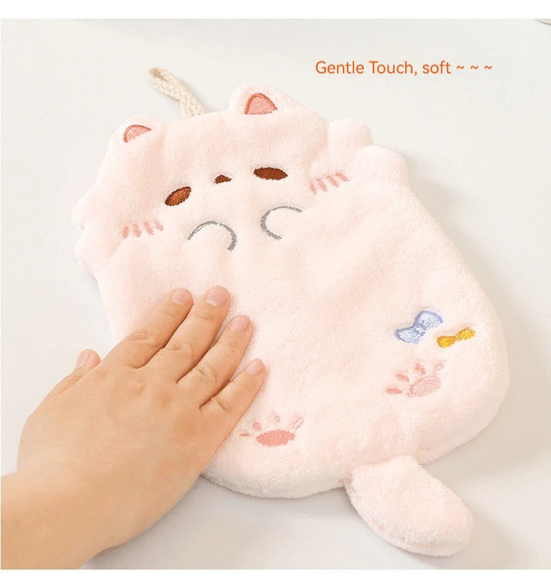 A hand touches a soft, pink KittyNook Cat Co. Cute Cat Hanging Towel with embroidered details on a white surface.