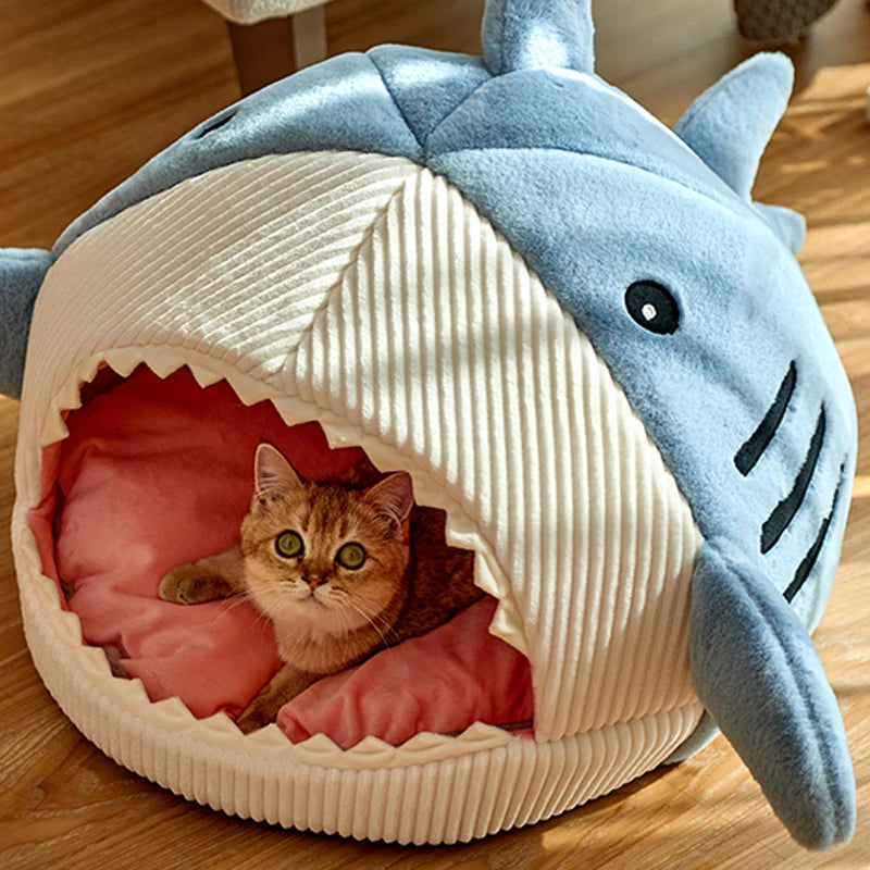 A cat peeks out from the Shark-Shaped Cat Cave Bed by KittyNook Cat Co., lounging on its cozy pink cushion.