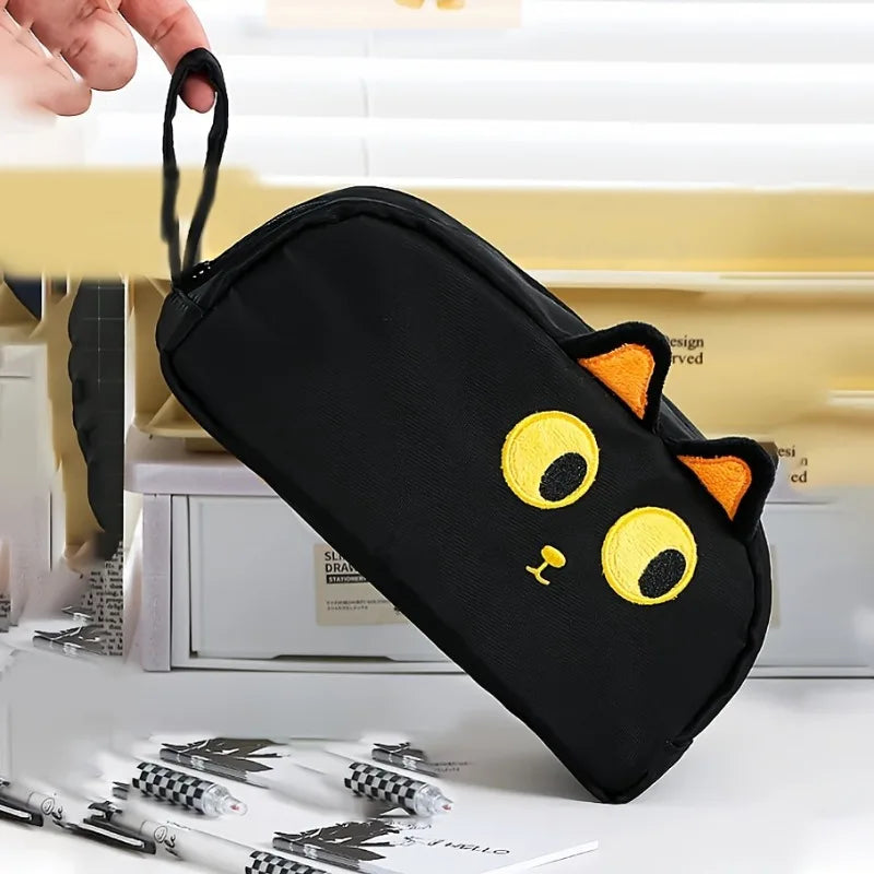 A hand holds the KittyNook Cat Co. Adorable 3D Cat Pencil Case with yellow eyes, orange ears, and a yellow nose.