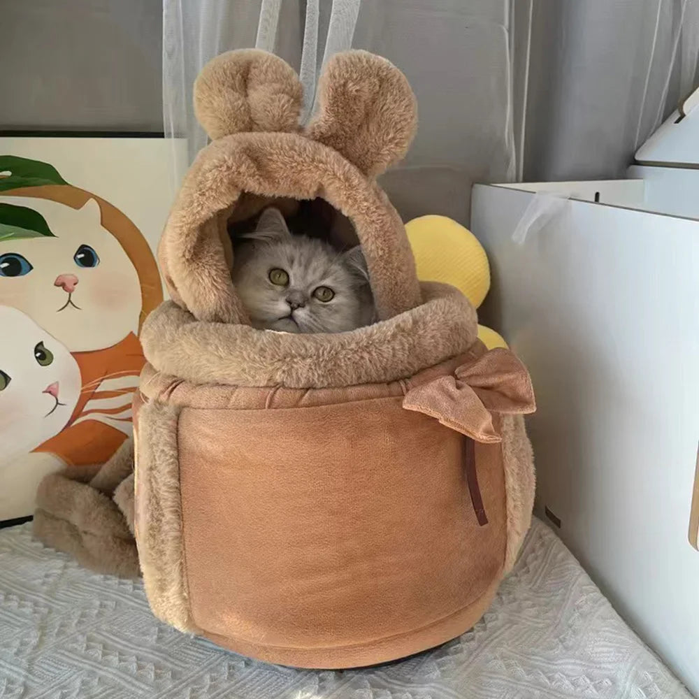 A fluffy gray cat sits in The Stylish Pet Travel Bag by KittyNook Cat Co., a cute, bear-shaped carrier with soft ears and bow.