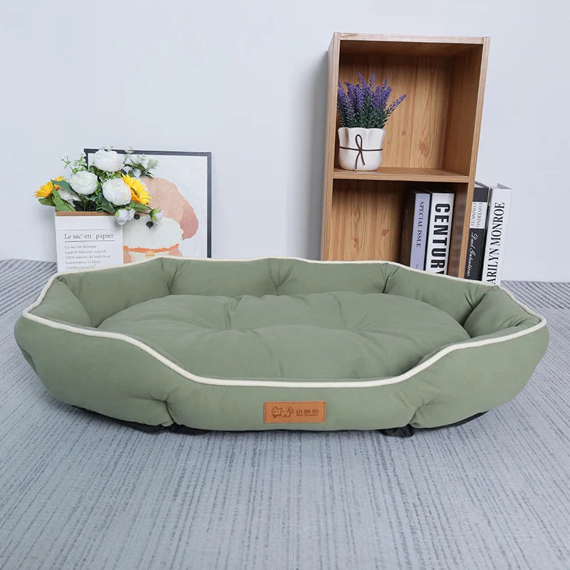 The Comfy Cat Sofa Sleeping Bed by KittyNook Cat Co. in green rests on a gray floor with shelves, books, and flowers.