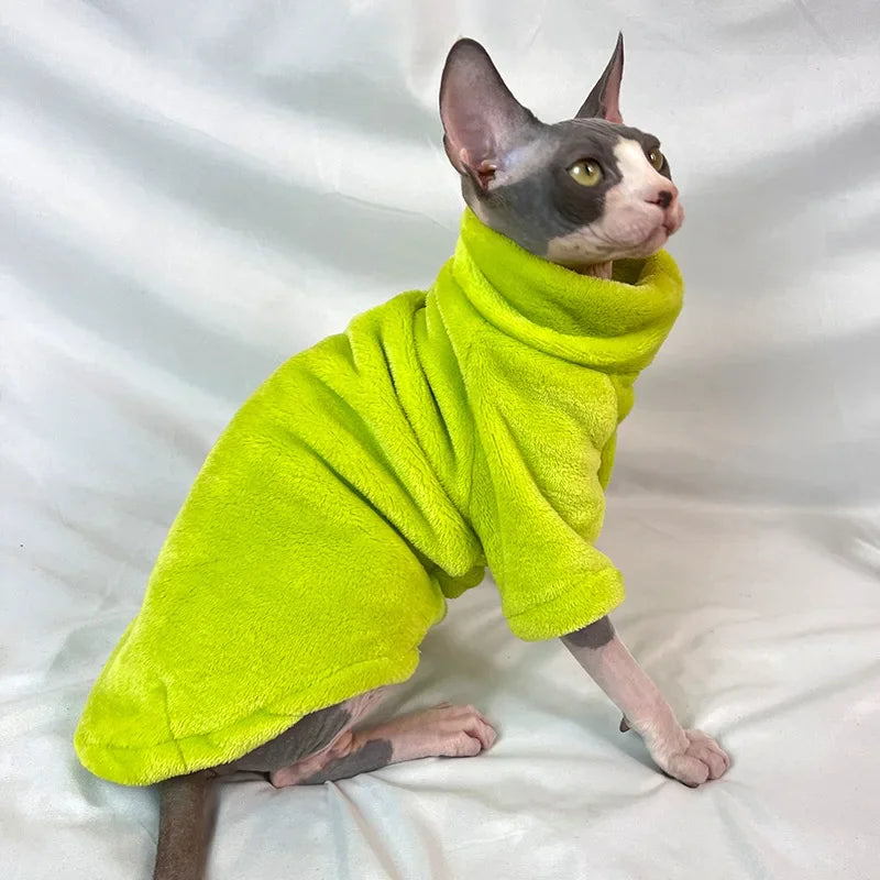 A sphynx cat wears a KittyNook Cat Co. Warm Winter Hoodie for Hairless Kittens, sitting on a white surface.