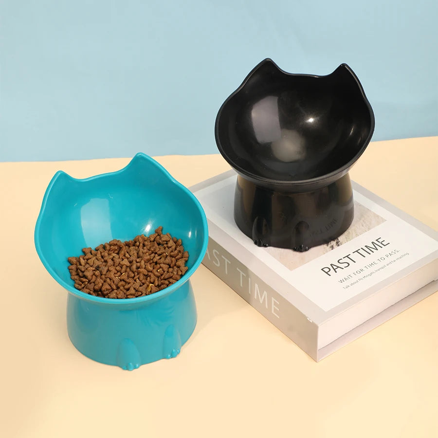 Two blue Orthopedic Raised Cat Feeders by KittyNook Cat Co. with kibble sit on a book against a pastel background.