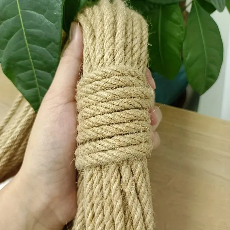 A hand holds the Purrfect Haven Natural Sisal Rope Scratcher by KittyNook Cat Co. with green leaves in the background.
