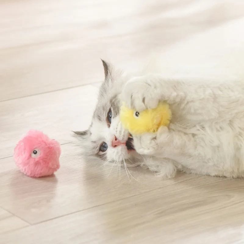 A fluffy white cat plays with the KittyNook Cat Co. Interactive Cat Smart Ball Toy; a pink plush adds extra enrichment.