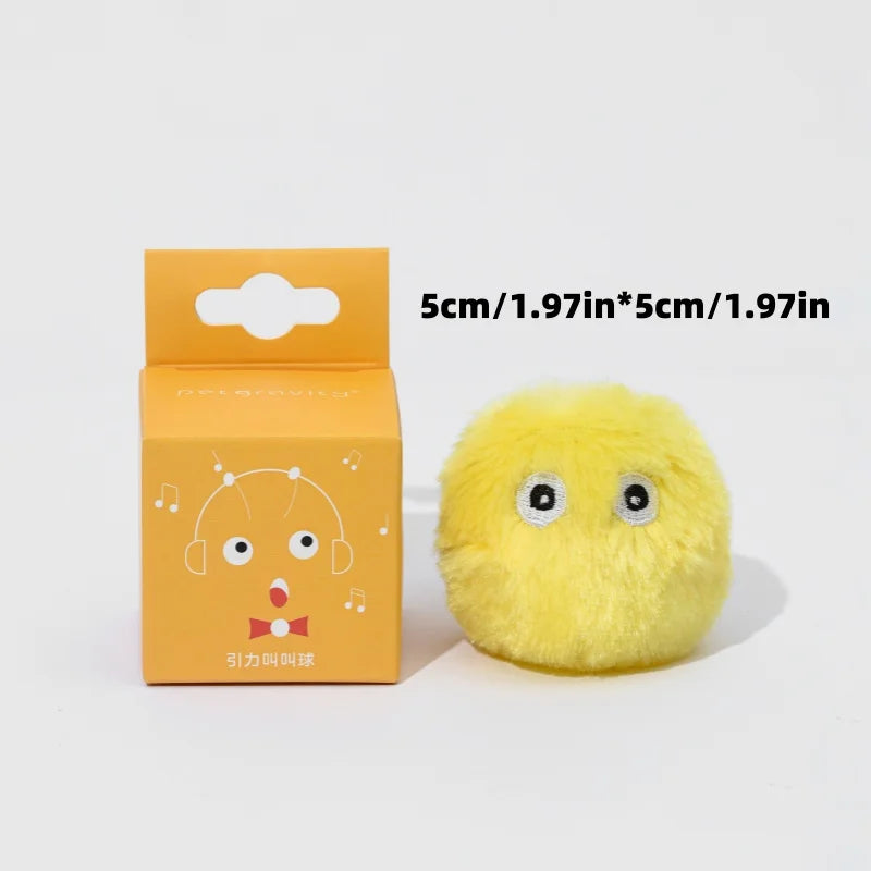 KittyNook Cat Co. Interactive Cat Smart Ball Toy: small, yellow, fluffy with eyes, near orange box with cartoon face.