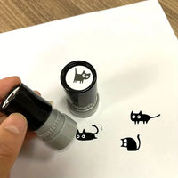 Thumbnail for A hand uses the KittyNook Cat Co. Black Cat DIY Journaling Stamp to print a kawaii black cat on white paper.