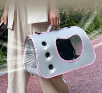 Thumbnail for A person carries the KittyNook Cat Co. Portable Pet Carrier Bag with mesh windows for comfy pet travel near green plants.
