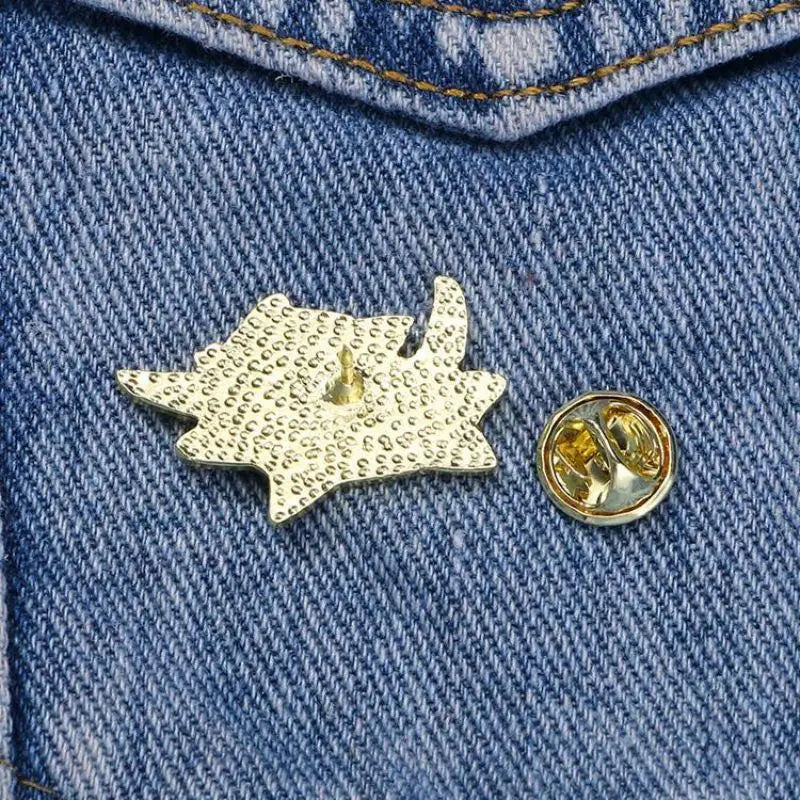 The KittyNook Cat Co. Cute Black Cat Enamel Brooch and its backing sit on blue denim with visible stitching.