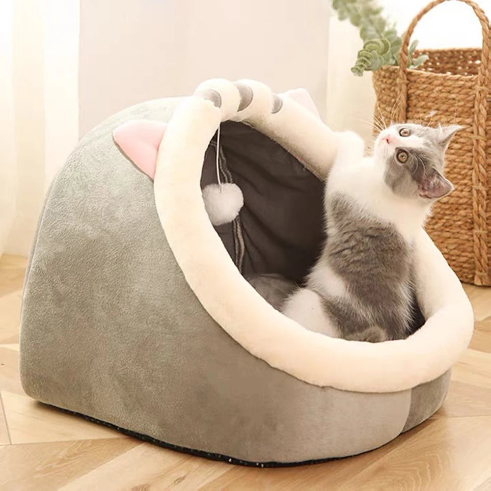 A gray and white cat plays in the KittyNook Cat Co. Cute Comfortable Cat Nest Bed on a wood floor near a basket.