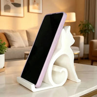 Thumbnail for A white Cute Cat Phone Stand – Adjustable Mobile & Tablet Holder holding a purple smartphone on a table.