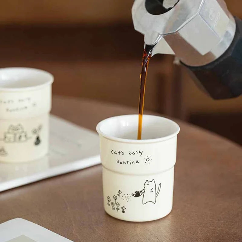 Coffee being poured from a moka pot into the KittyNook Cat Co. Cute Illustrated Ceramic Cat Mug with cat designs.