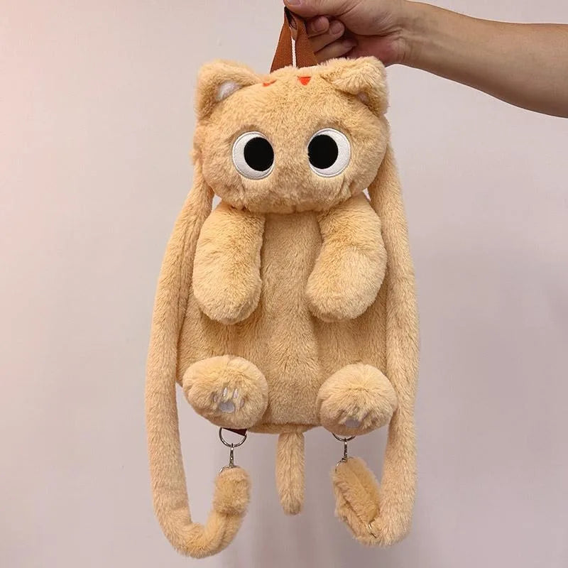 A hand holds KittyNook Cat Co.'s The Cute Big Eyes Plush Backpack, shaped like a cat with long arms and a tail.