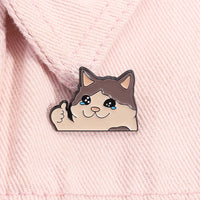 Thumbnail for KittyNook Cat Co.'s Kawaii Thumbs Up Crying Cat Enamel Pin on pink fabric—purrfect for cute cat fans!.