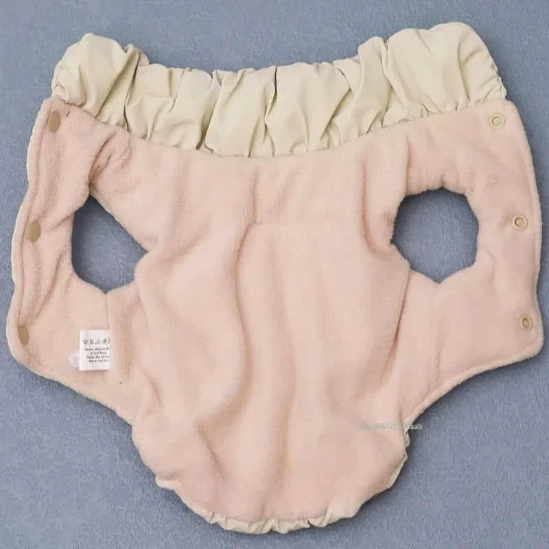 The KittyNook Cat Co. Ultra-Soft Padded Winter Cat Jacket in beige, with snap buttons, laid flat on a blue surface.