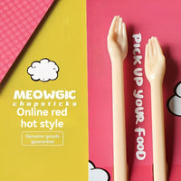 Thumbnail for Little Paws Silicone Training Chopsticks for Kids by KittyNook Cat Co. beside “Pick up your food” on pink and yellow.