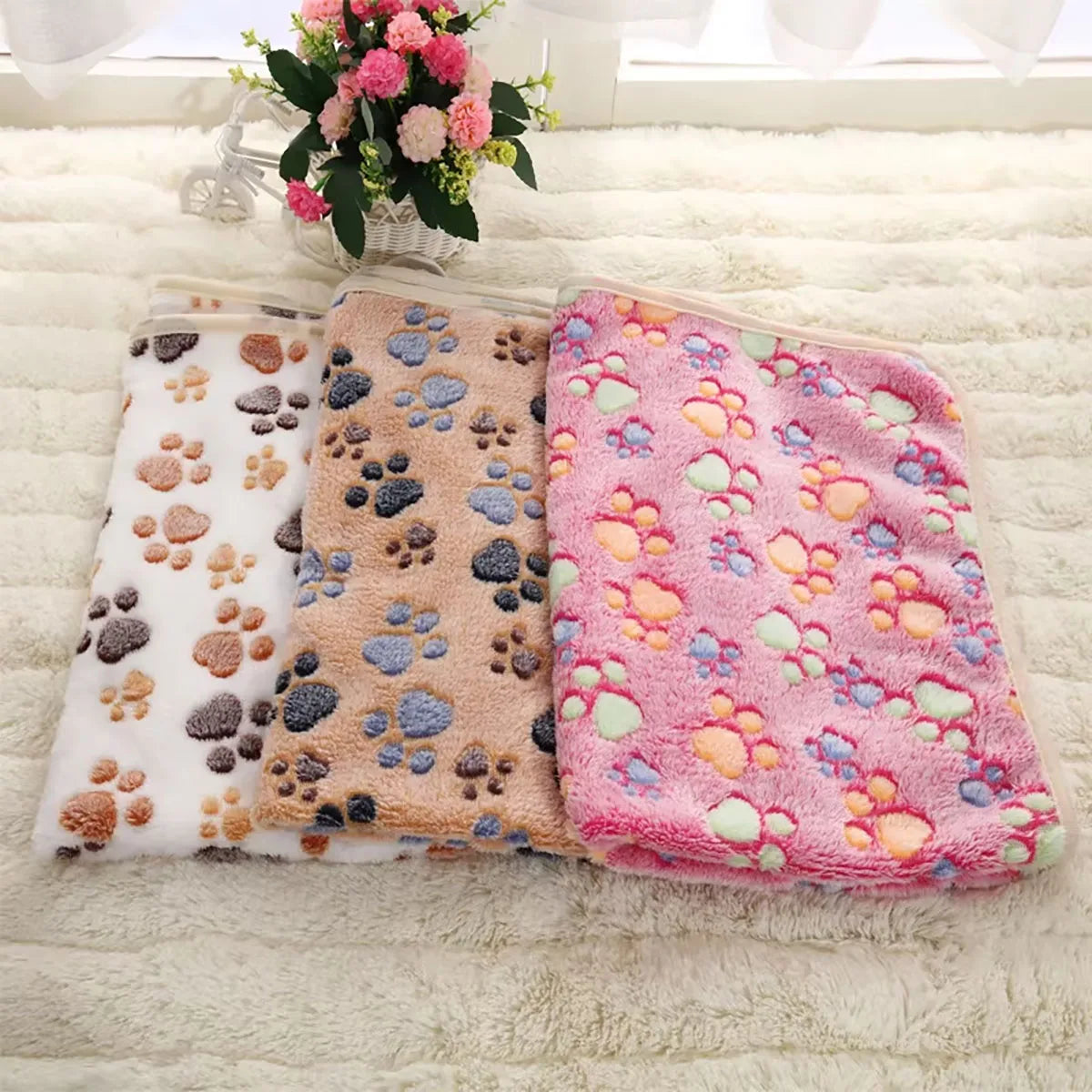 Three SnugglePaws Luxe Fleece Pet Blankets by KittyNook Cat Co. with paw prints are displayed on a plush surface.