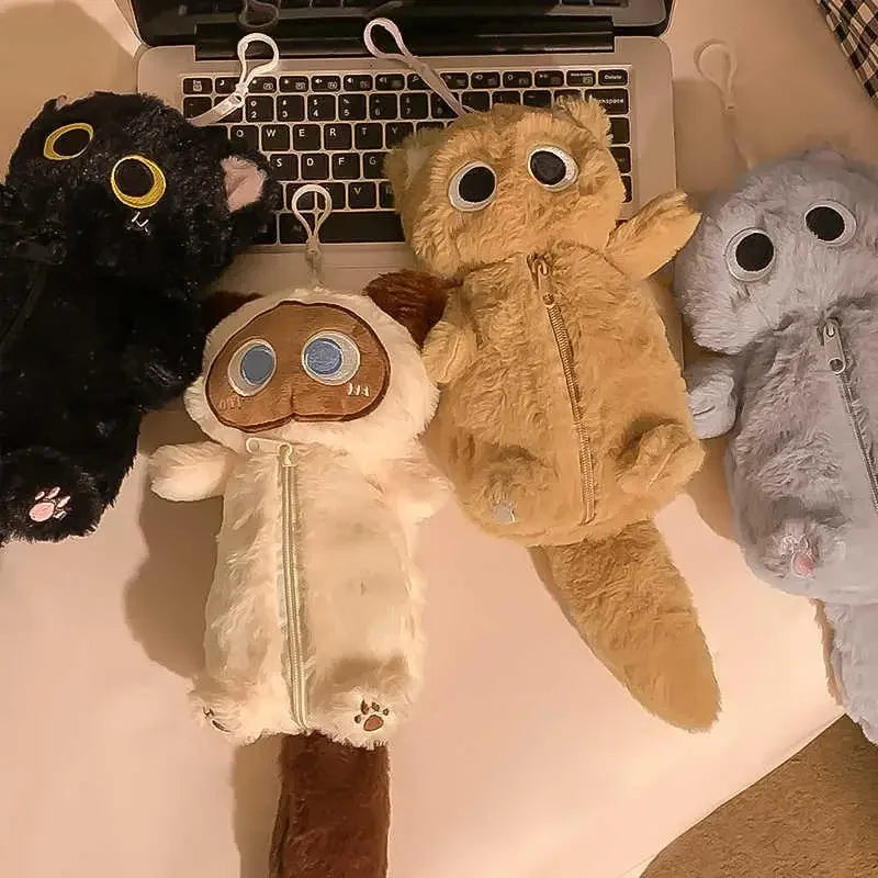 Four KittyNook Cat Co. Kawaii Big-Eyed Cat Plush Pencil Cases are arranged on a desk in front of a laptop keyboard.