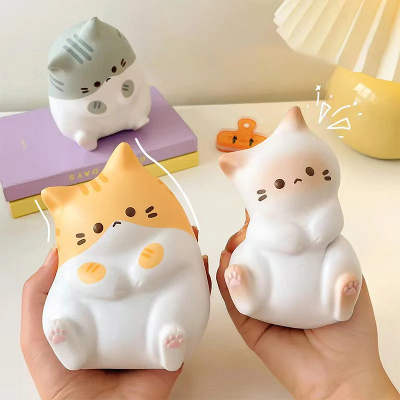 Two hands hold KittyNook Cat Co. Cat Squeeze Balls; another sits on a purple box in the background.