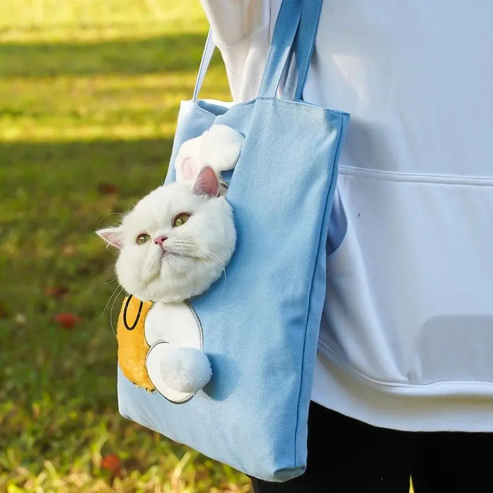 A white cat peeks from a KittyNook Cat Co. Portable Crossbody Cat Carrier Bag, worn on grass by someone in white.