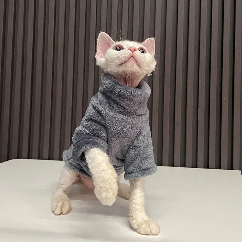 A hairless cat in KittyNook Cat Co.'s Warm Winter Hoodie for Hairless Kittens stands on a white surface, paw raised.