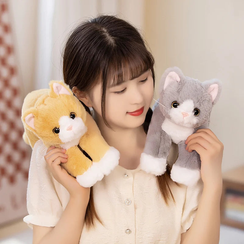 A young woman smiles, holding a KittyNook Cat Co. Snuggle Soft Cat Plush Doll and a gray plush cat.