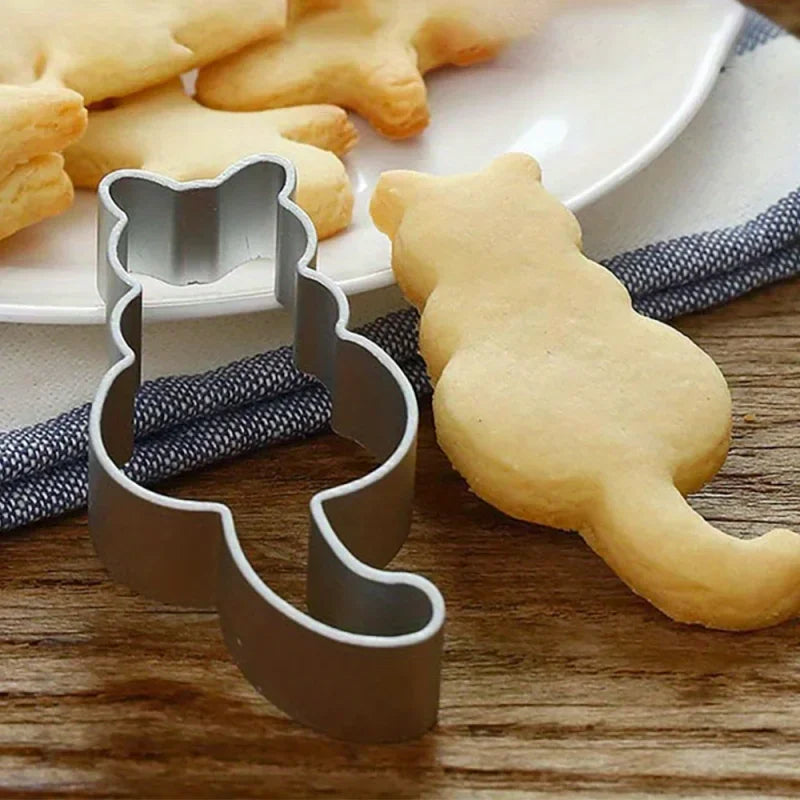 KittyNook Cat Co. Cat Shape Cookie Cutter Set with cat-shaped cookie beside a plate on a wooden table.