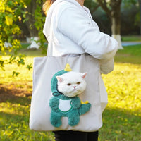 Thumbnail for A person carries a KittyNook Cat Co. Portable Crossbody Cat Carrier Bag; a cat peeks out in a green dinosaur costume.