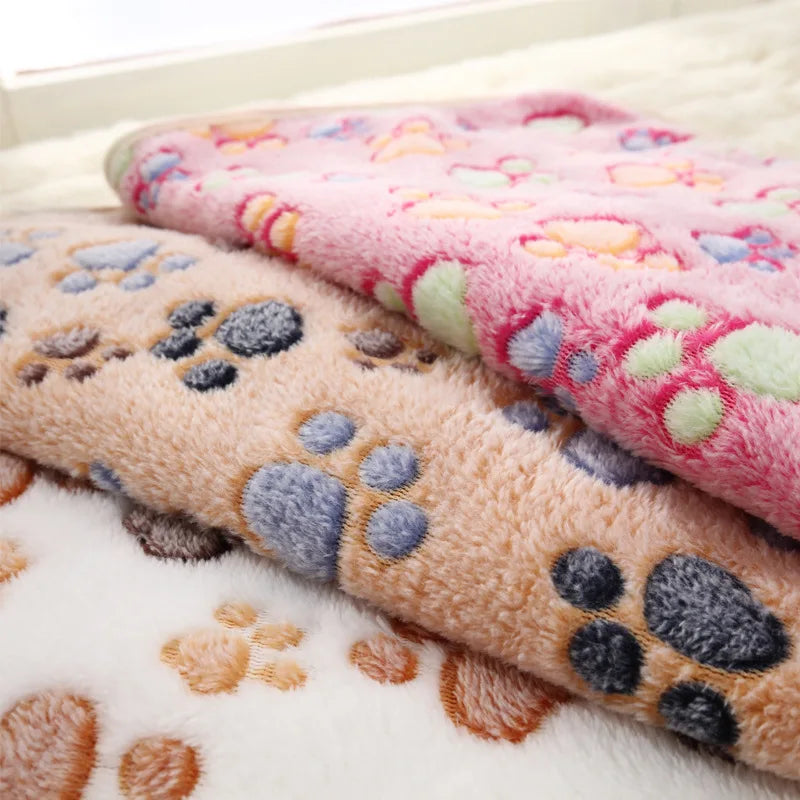 Three SnugglePaws Luxe Fleece Pet Blankets by KittyNook Cat Co. with colorful paw prints stacked together.