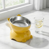Thumbnail for Yellow Elevated Cat Food Bowl with Cute Ear Stand containing a stainless steel insert, next to a glass of lemon water.