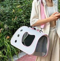 Thumbnail for A woman outdoors carries the KittyNook Cat Co. Premium Foldable Small Cat Carrying Bag in white and pink.