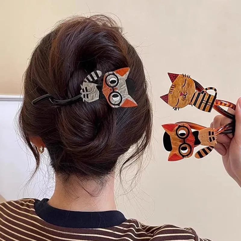 A woman with a bun wears The Acrylic Cat Hairpin by KittyNook Cat Co. and holds two more cat hair accessories.