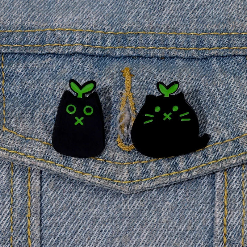 Two KittyNook Cat Co. Black Cat Enamel Brooches with green sprouts add cute flair to any denim jacket for cat lovers.
