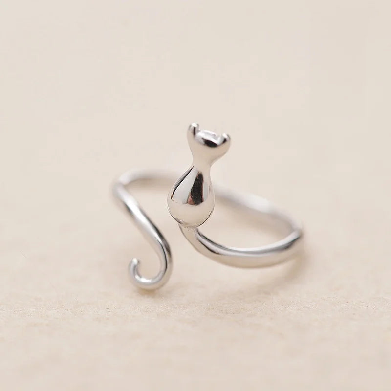 The Cute Adjustable Silver Cat Ring by KittyNook Cat Co., a minimalist curled tail piece, on a beige background.