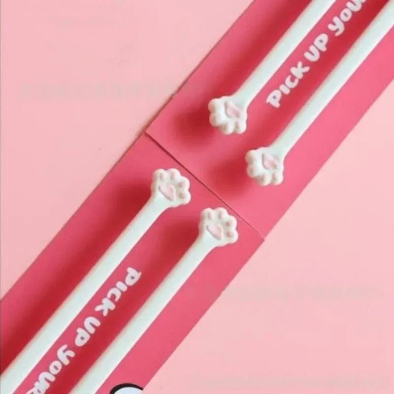 Four white Little Paws Silicone Training Chopsticks by KittyNook Cat Co. with cat paw tips on a pink background.