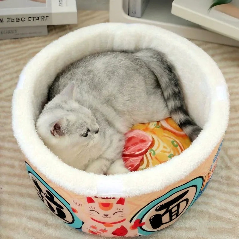 A gray cat curls up in the KittyNook Cat Co. Giant Ramen Bowl Cat Bed with colorful lucky cat patterns.